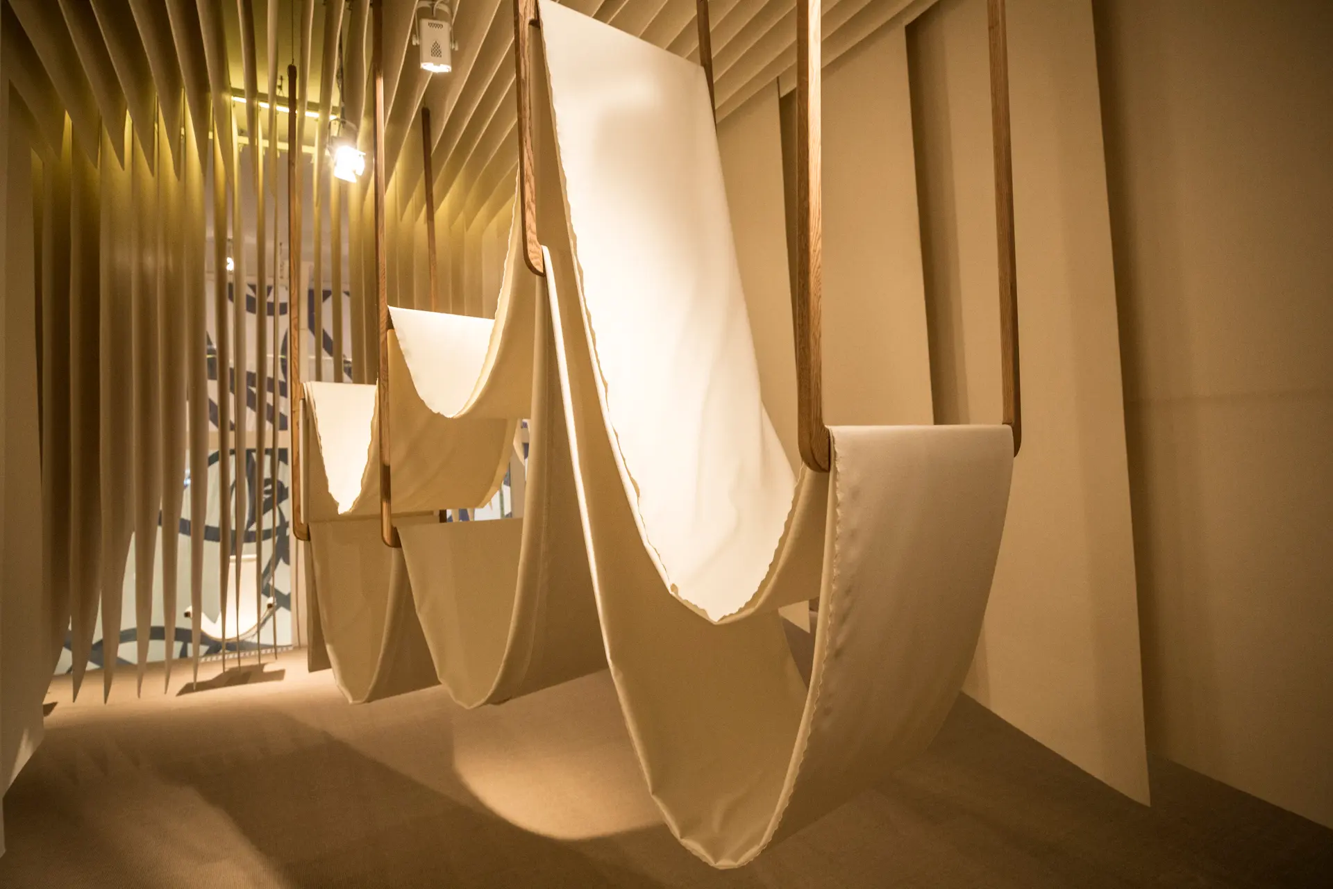 Fabric suspended within a softly lit installation space, framed by layered vertical panels.
